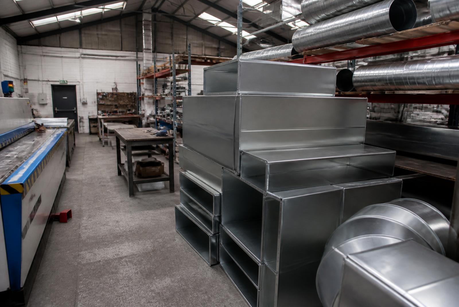 Fabricated galvanised rectangular duct sections and spiral ductwork stacked in a sheet metal workshop