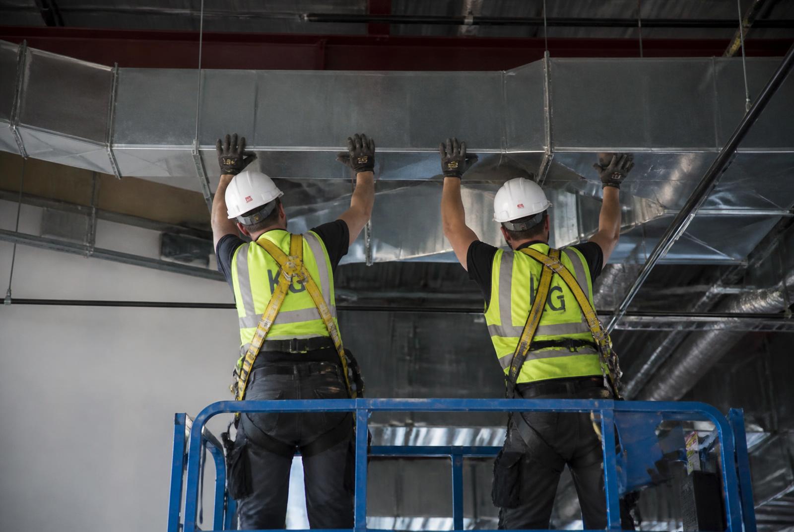 Ductwork installers fitting galvanised rectangular ductwork from a scissor lift on a commercial fit-out